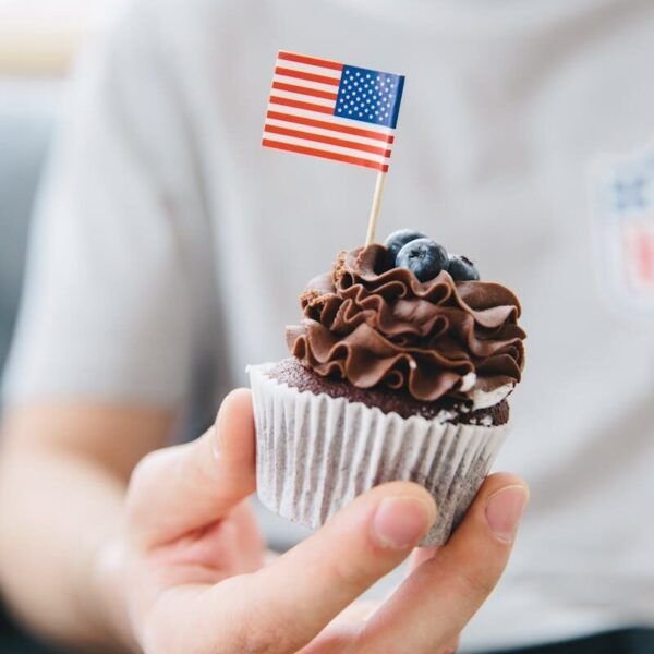 Delicious chocolate cupcake with blueberry topping adorned with an American flag, held in hand.